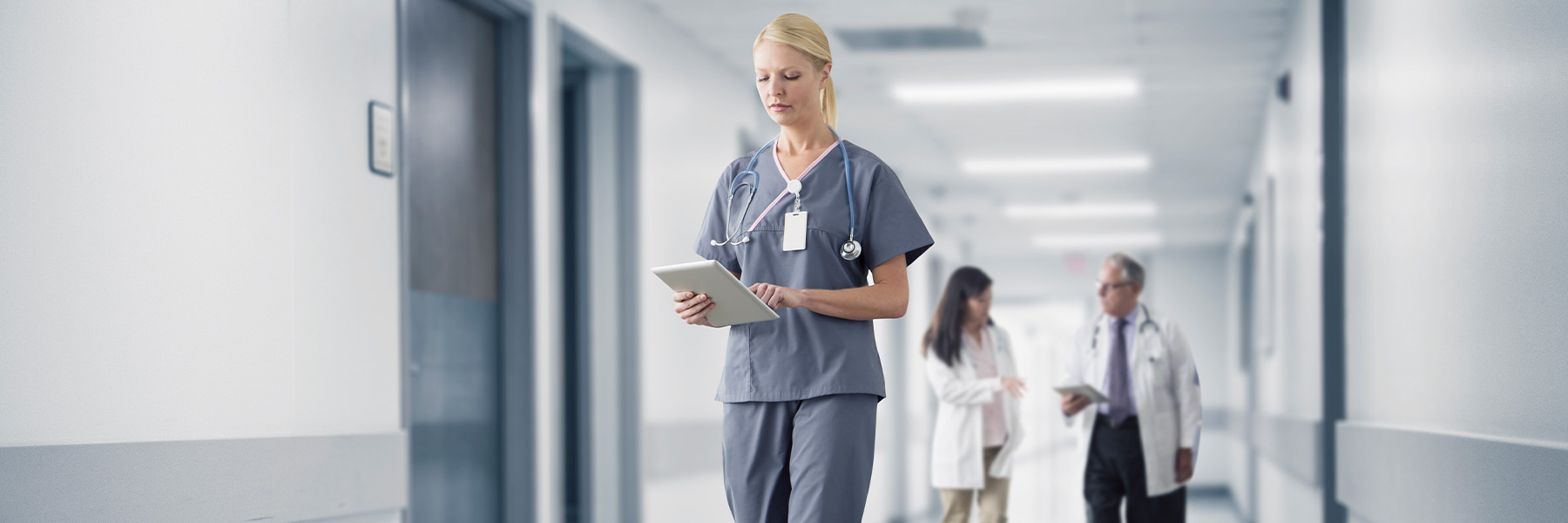 A nurse looks at a tablet as she walks down the hallway of a hospital. 
