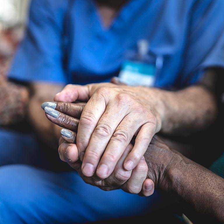 A close-up of a nurse holding a patient’s hands