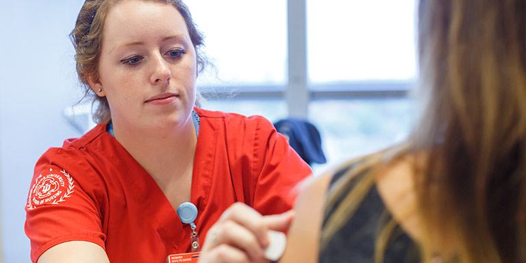 A nurse in red scrubs gives a patient a shot.